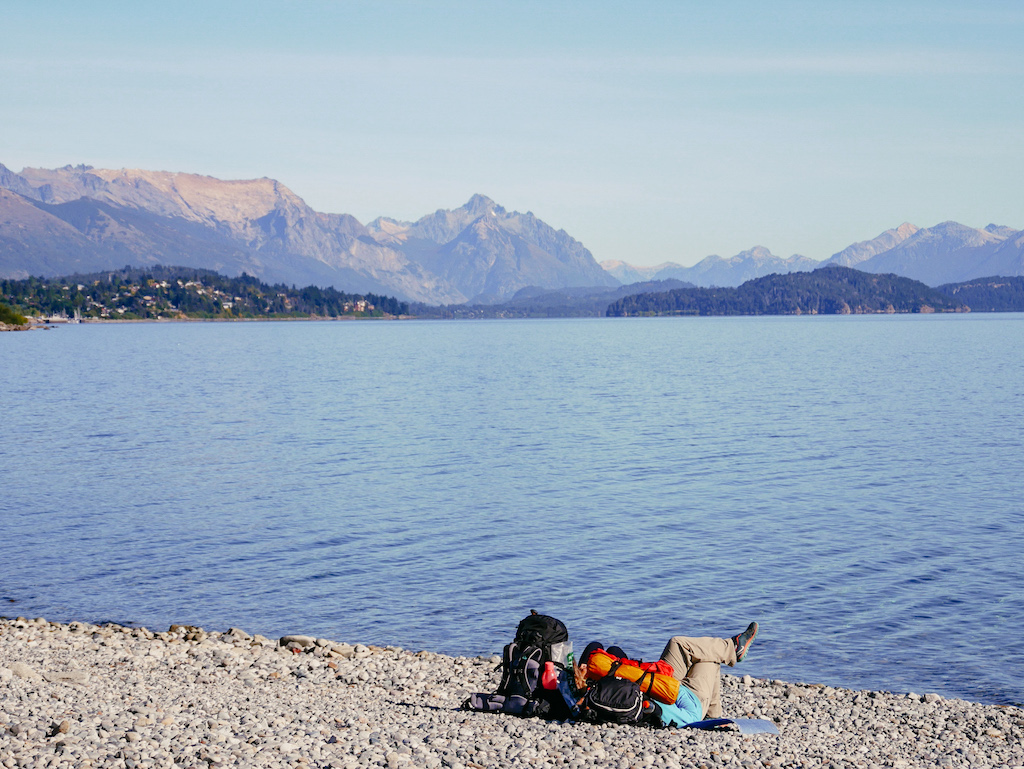Argentinien, Person liegt am See mit einem Rucksack mit Bergpanorama