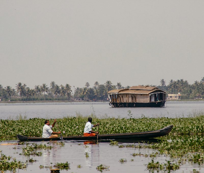 Zwei Fischer auf einem Kanu und ein Hausboot auf dem Fluss in den Backwaters von Kerala