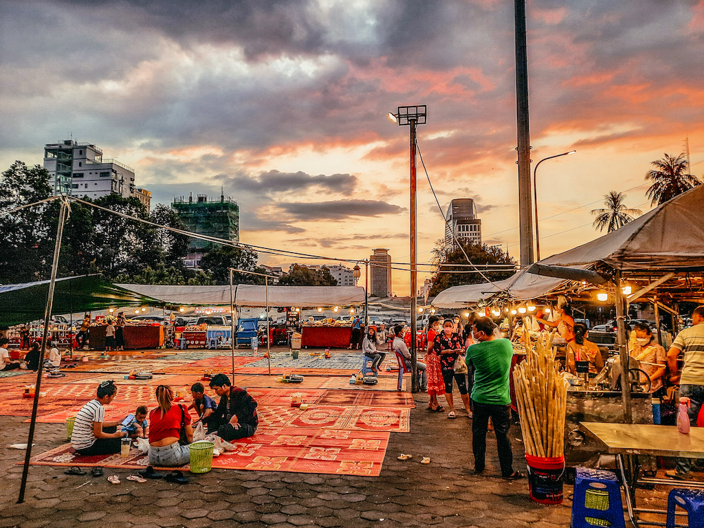 Nachtmarkt, Menschen stehen an ständen und sitzen auf dem Boden